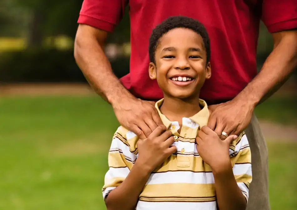 En leende pojke står framför sin pappa som håller sina händer på pojkens axlar.