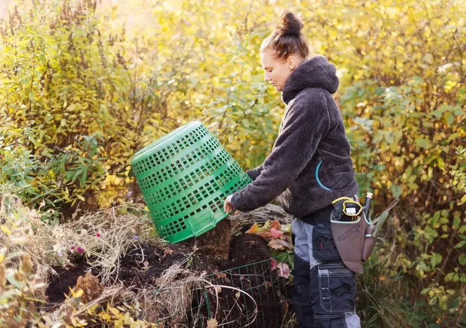 Kvinna i arbetskläder tömmer innehållet i en lövkorg på en kompost